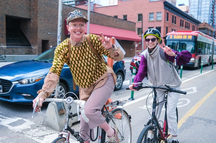 Two festival attendees smile for the camera as they ride their bikes down a bike lane.
