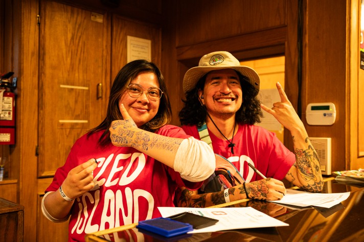 Two volunteers wearing red Sled Island t-shirts smile for the camera while working the front door at the #1 Royal Canadian Legion during Sled Island 2024.