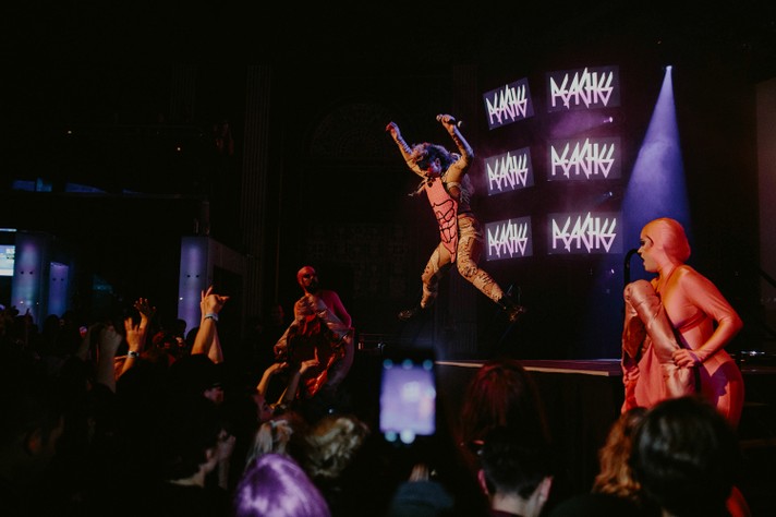 The artist Peaches jumps off a riser with their arms in the air during a performance at The Palace Theatre during Sled Island 2016.