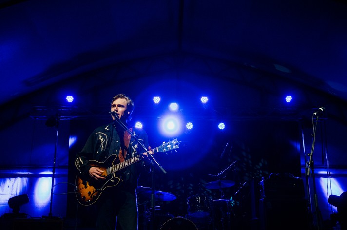 Artist Joel Plaskett is shown singing and playing guitar at Olympic Plaza during Sled Island 2014. Blue stage lights shine behind him.