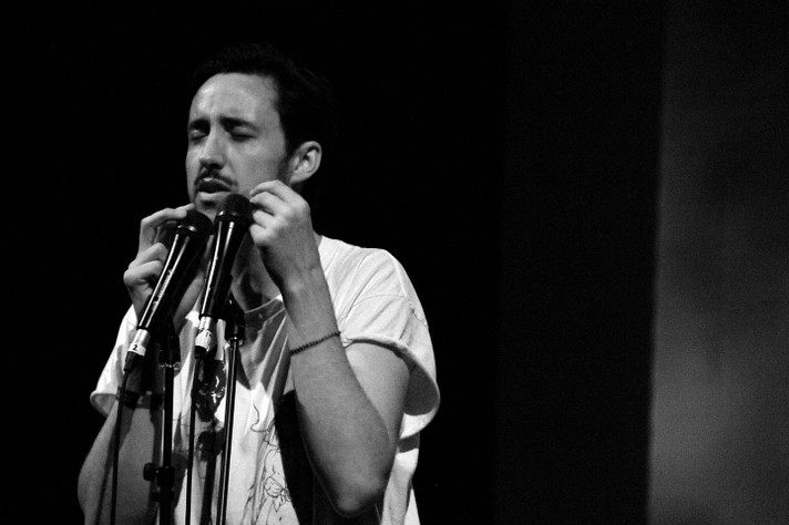 A black and white photo shows Tom Krell of the project How to Dress Well wearing a white t-shirt singing while touching their face as they perform at Theatre Junction Grand during Sled Island 2012.