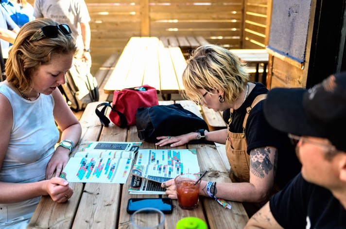 Two festival attendees sit at a picnic table and take look at the schedule in the program guide during Sled Island 2024.