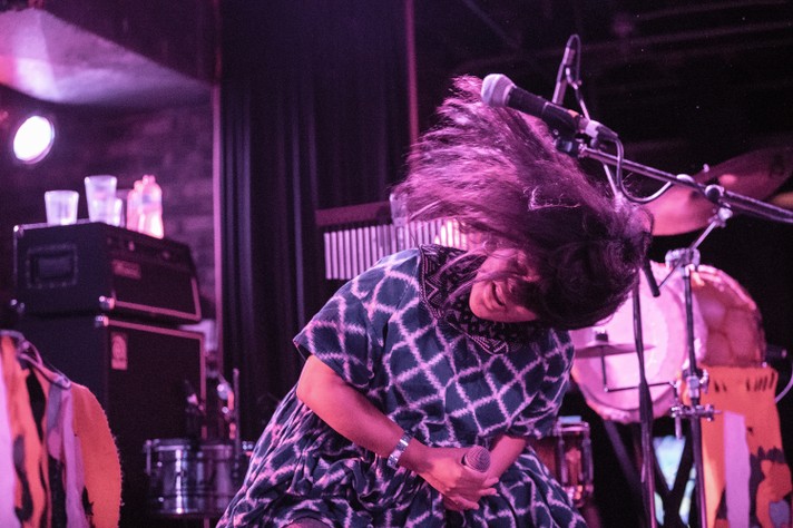Artist Lido Pimienta is seen in blue and white checkered dress flipping their hair around on stage at Commonwealth Bar & Stage during Sled Island 2018.