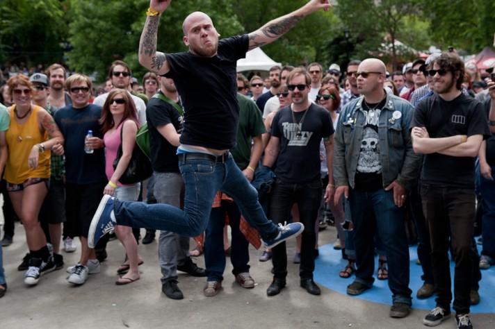 The frontperson of the group The Bronx is shown in the middle of the audience jumping in the air wearing a black t-shirt and blue jeans during their performance at Olympic Plaza for Sled Island 2010.