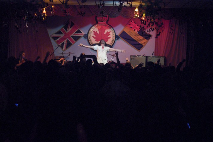 Artist Andrew W.K. is shown on stage at the #1 Royal Candian Legion during Sled Island 2009. He is dressed all in white with a signature blood stain on the front of his shirt, and has his arms outstretched in a cross formation..