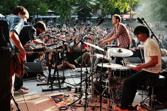 The four members of the group perform while facing each other at Olympic Plaza during Sled Island 2009. The photo is taken from the stage and the audience can be seen in the background.