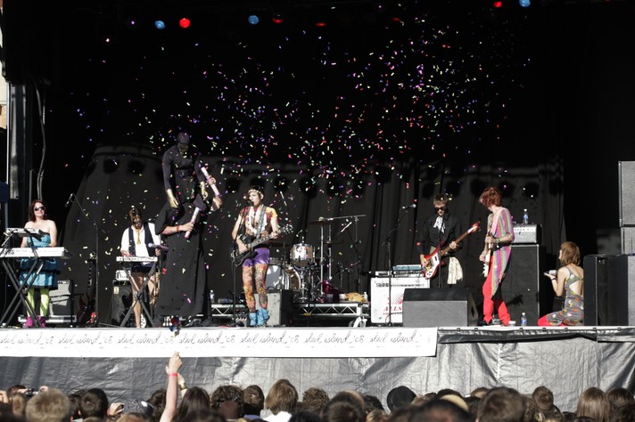 The group Of Montreal performs at Shaw Millenium Park during Sled Island 2008. A mysterious figure, which appears to be someone on the shoulders of another person, all dressed in black, shoot confetti in the air.