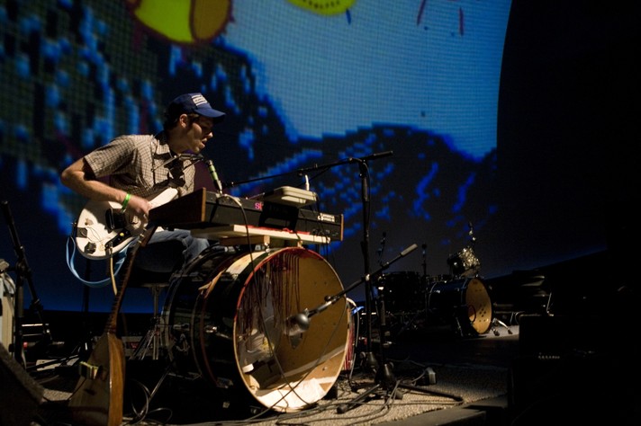 Artist Chad VanGaalen is seen playing guitar and singing while sitting behind a bass drum with a keyboard mounted on top during their performance at Telus World of Science for Sled Island 2008.
