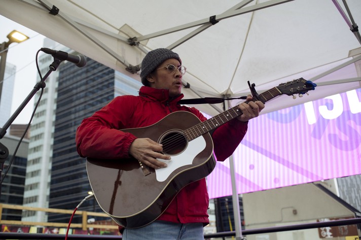 Artist Wyatt C. Louis is shown playing acoustic guitar at High Park for Camp Sled Island in 2021. He is wearing a red jacket and grey toque.