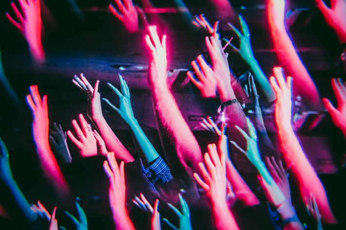 Arms are outstretched in the crowd bathed in pink and blue lights during Sled Island 2024