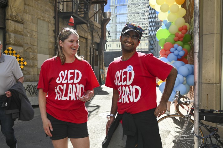 Two volunteers in red Sled Island t-shirts smile for the camera at Sled Alley during Sled Island 2024.